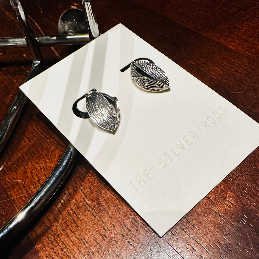 Silver leaf-shaped earrings on a white card with 'The Silver Box' branding on a wooden surface.
