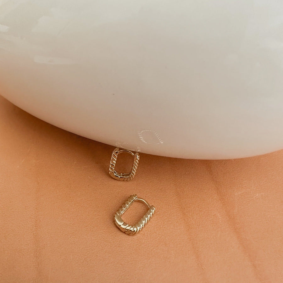 Gold hoop earrings on a person's earlobe with a white background