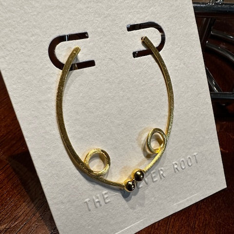 Gold earrings on a branded card, placed on a wooden surface.