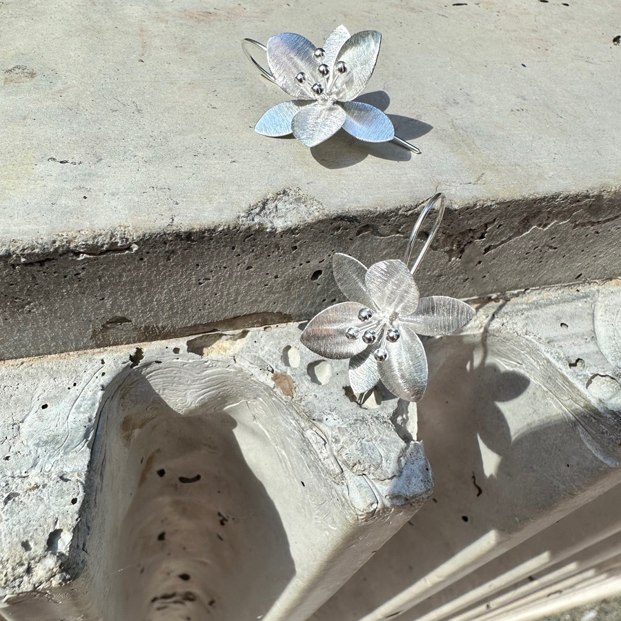 Silver flower-shaped earrings on a textured stone surface